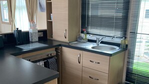 A compact kitchen with a sink, cabinets, and a window with blinds. - VALENCIA 2 BEDROOMS LAKESIDE LODGE (Weeley)