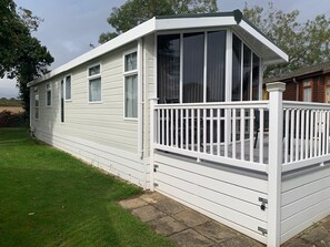 Una casa mobile con esterno bianco, un portico coperto e un piccolo giardino antistante.