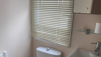 A small bathroom with a toilet, a sink, and a window with blinds.