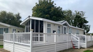 A white mobile home with a fenced deck and a staircase leading to the entrance. - VALENCIA 2 BEDROOMS LAKESIDE LODGE (Weeley)