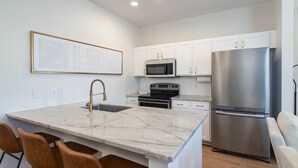 A modern kitchen with white cabinets, stainless steel appliances, a marble countertop, and a built-in island with bar stools. - Colonel's Cottage Oxford - 2mi to The Square (Oxford)