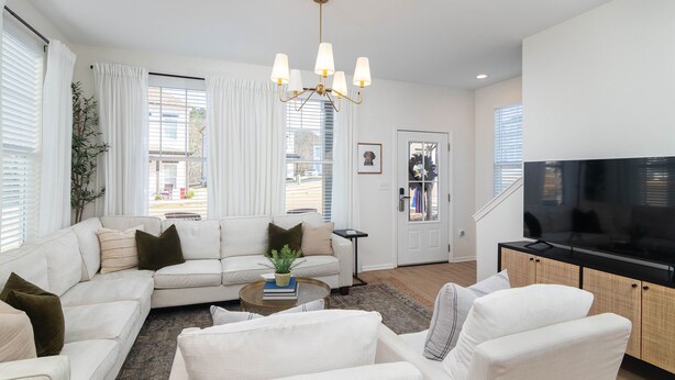 A modern living room with a sectional sofa, a coffee table, a TV on a wooden cabinet, and a chandelier. - Colonel's Cottage Oxford - 2mi to The Square (Oxford)