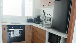 A compact kitchen with wooden cabinets, a built-in oven, a coffee maker, and a refrigerator.