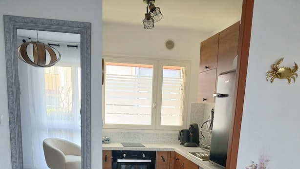 A modern kitchen with wooden cabinets, a built-in oven, and a coffee maker. There is a dining table with chairs and a vase of flowers.