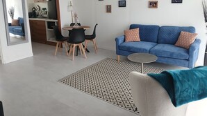 A modern living room with a blue sofa, black chairs, a small round table, and a kitchen in the background.