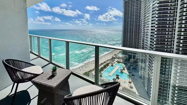 A balcony with wicker furniture, a view of the ocean, and a resort area with a pool. - Enjoy a luxurious apartment on the beach! (Hollywood)