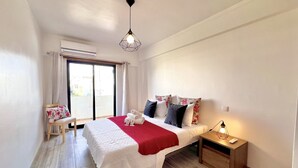 Una habitación de hotel con cama, mesita de noche, ventana con cortinas e iluminación en el techo.