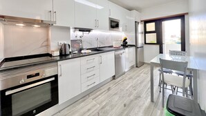 Una cocina moderna con armarios blancos, horno de acero inoxidable, microondas y refrigerador. Hay una mesa de comedor con sillas y una ventana con vistas.