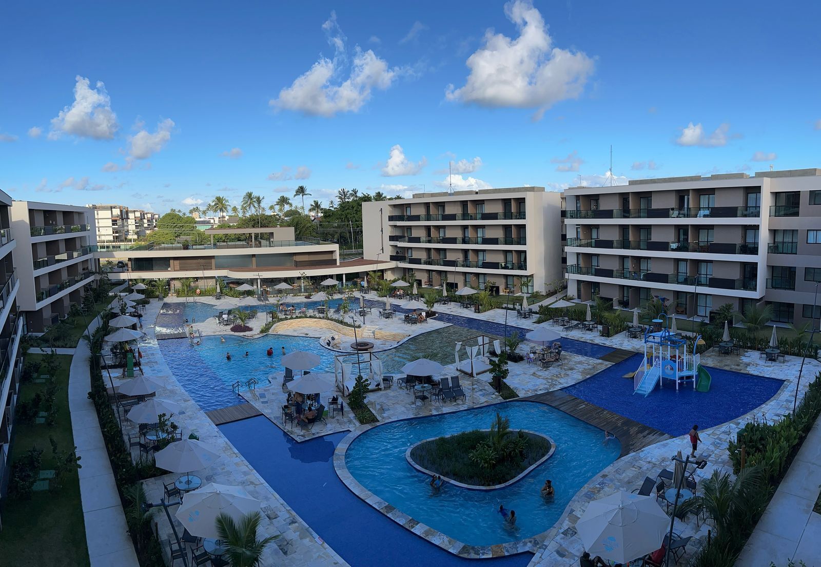 A resort with multiple swimming pools, outdoor seating, and a view of the surrounding buildings.