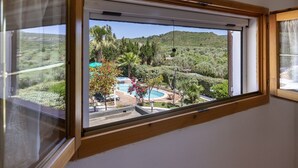 A room with a large window overlooking a pool area with trees and hills. - Villa Piccola Stella with attached annex and private pool (Sardegna)
