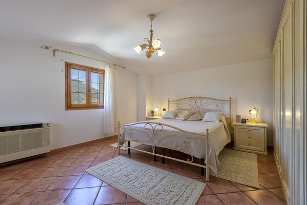 A bedroom with a bed, bedside tables, a radiator, a window, and a chandelier.
