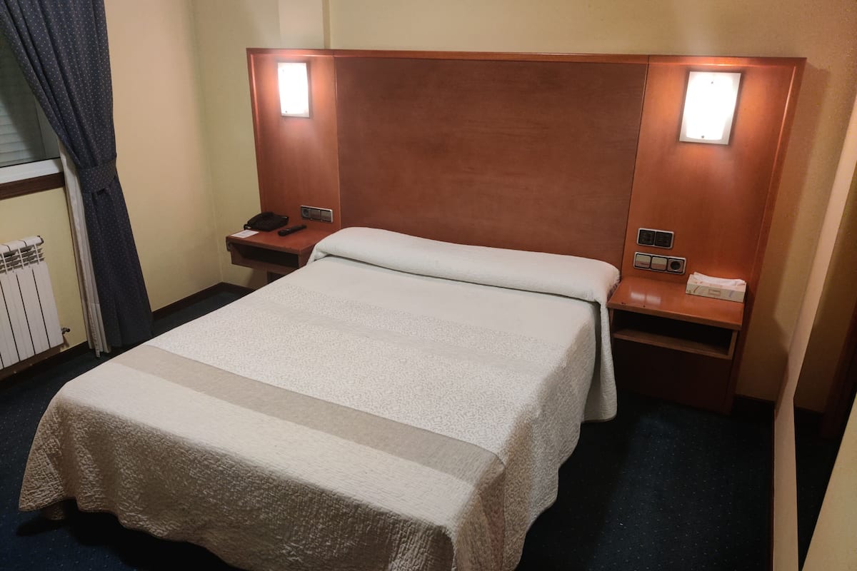 Een hotelkamer met een bed, nachtkastje, telefoon en een bedieningspaneel aan de muur.