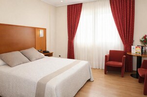 Habitación de hotel con cama, mesita de noche, una mesa con silla y ventana con cortinas.