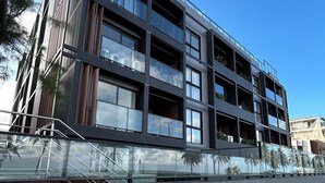 A modern multi-story building with balconies, large windows, and a paved walkway.
