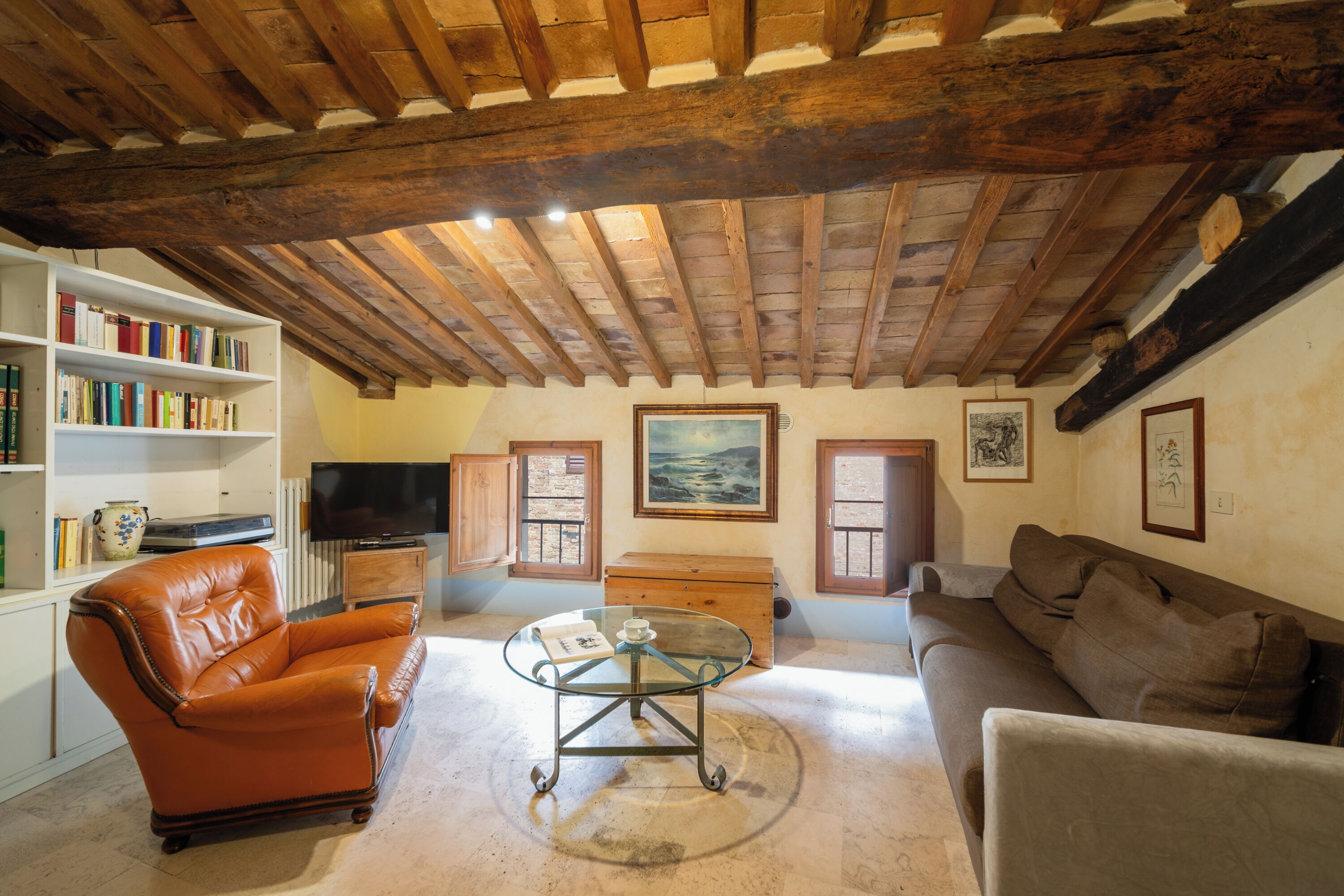 Ein gemütliches Wohnzimmer mit Ledersessel, Glastisch, Sofa, Bücherregal und Fernseher.