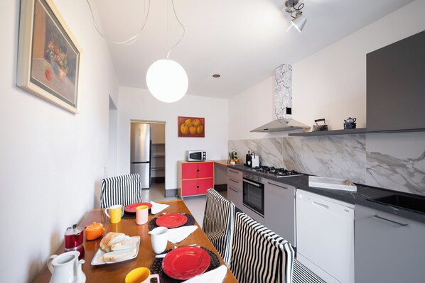 A modern kitchen with a dining area, featuring a marble backsplash, stainless steel appliances, and a red cabinet.