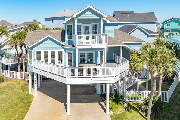 A multi-story house with a balcony, a covered porch, and a small garden area with palm trees. - 2nd Row in Pirates Beach, Great Gulf Views, Steps from Beach, Updated Interior (Galveston)