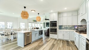 Une cuisine moderne avec des meubles blancs, un îlot central, des appareils en acier inoxydable et un pare-feu orné de carreaux bleus.