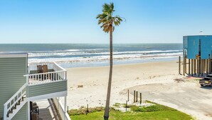 Une vue sur la plage depuis un balcon, avec un palmier, une plage de sable et l’océan.