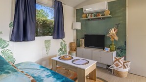 A room with a bed, a table with decorative items, a television, and an air conditioning unit.