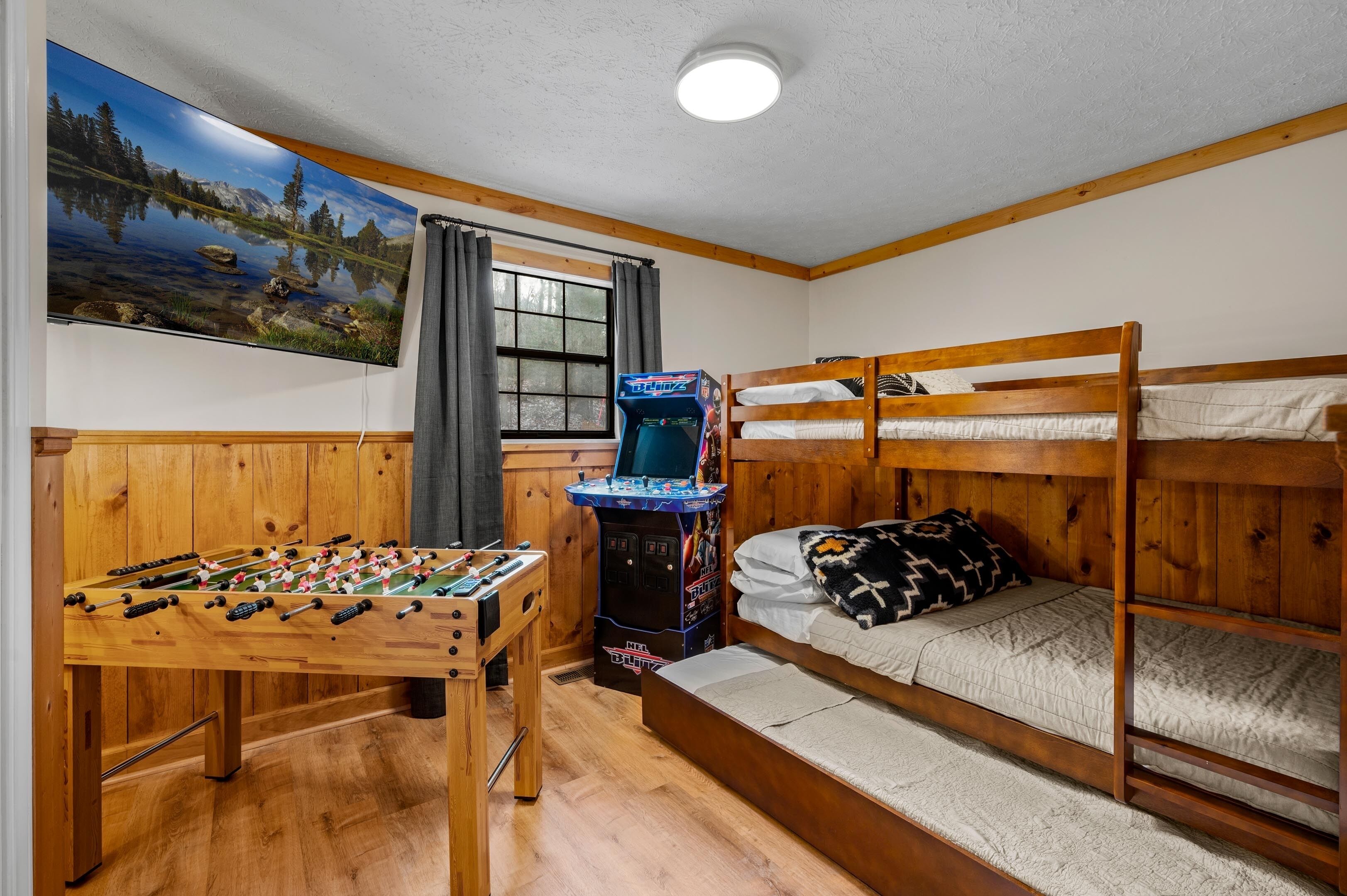 A room with a wooden bunk bed, a foosball table, and a Nintendo 64 arcade machine.