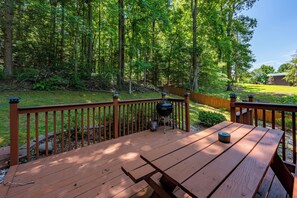 A wooden deck with picnic tables and a barbecue grill, surrounded by a forested area. - No Clean Fee! Hot Tub, Game Room, close to National Park and Pigeon Forge! (Sevierville)