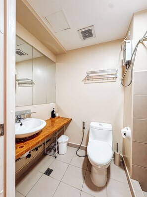 A bathroom with a wooden vanity, a white sink, a toilet, and a shower. - A Modern Zen Hideaway (Iloilo)
