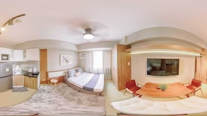 A modern hotel room with a curved bed, a kitchenette, a dining area with a wooden table and red chairs, and a large window. - Your Ultimate Studio Escape (Iloilo)