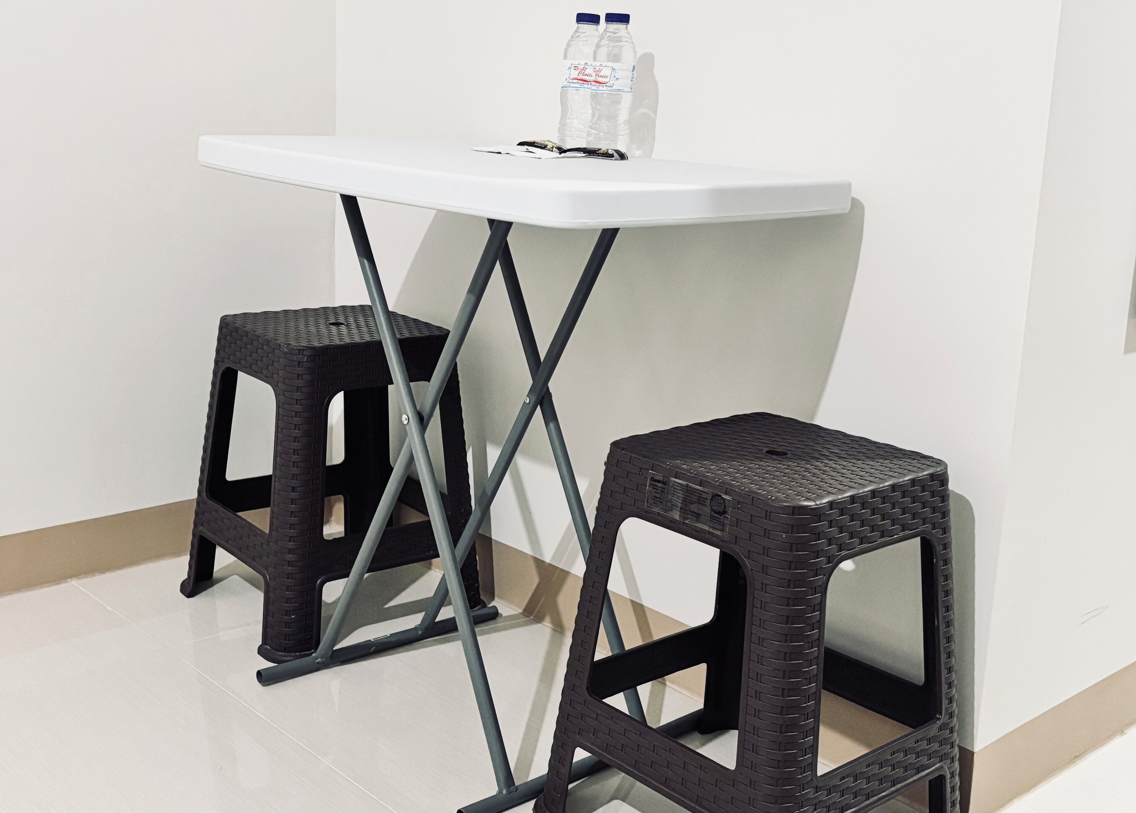A white table with two black stools, a bottle of water, and a pair of sunglasses on the table.