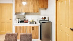 A compact kitchen with wooden cabinets, a microwave, a sink, and a refrigerator. - Cozy Family Suite Retreat (Iloilo)