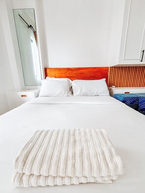 A neatly made bed with white linens and a white throw blanket, a wooden headboard, and a large mirror on the wall. - A Minimalist Urban Retreat (Iloilo)