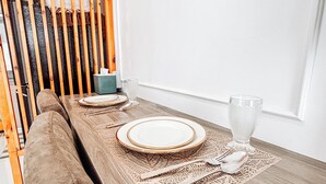 Une table à manger, dressée avec des assiettes, des couverts et un verre, avec un banc rembourré et une chaise en bois à lattes sur un côté.