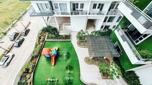 Un immeuble résidentiel à plusieurs étages, doté de balcons, d’un jardin sur le toit et d’un espace de jeux pour enfants.