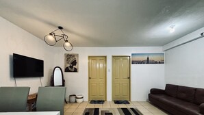 Ein Wohnzimmer mit Flachbildfernseher, einer Couch, einem Couchtisch, einem Teppich und zwei Türen.