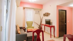 A living room with a sofa, a green armchair, a red chair, a TV on a wooden table, and a door. - Spacious & Cozy Urban Oasis (Iloilo)