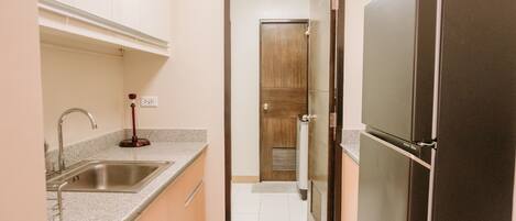 A kitchen with a stainless steel sink, a refrigerator, and a wooden door in the background.