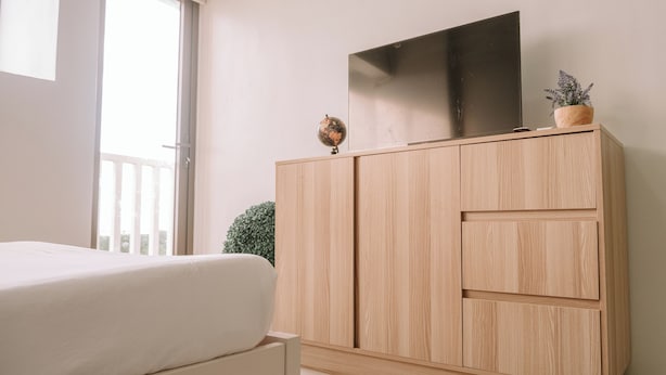 Un dormitorio con una cama, un armario de madera, un televisor de pantalla plana y una pequeña planta en maceta.