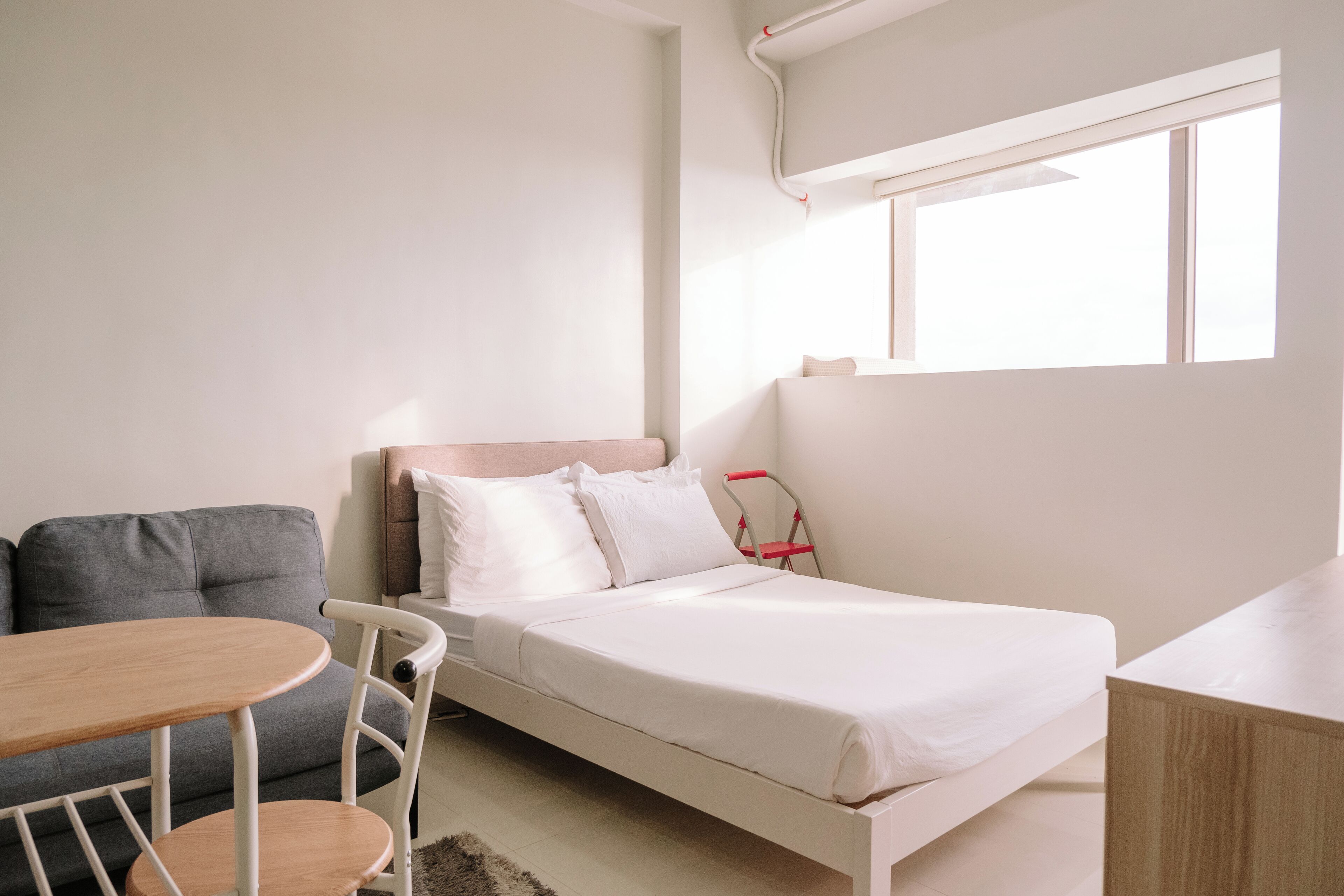 A bedroom with a bed, a gray sofa, a small round table, and a window with blinds.