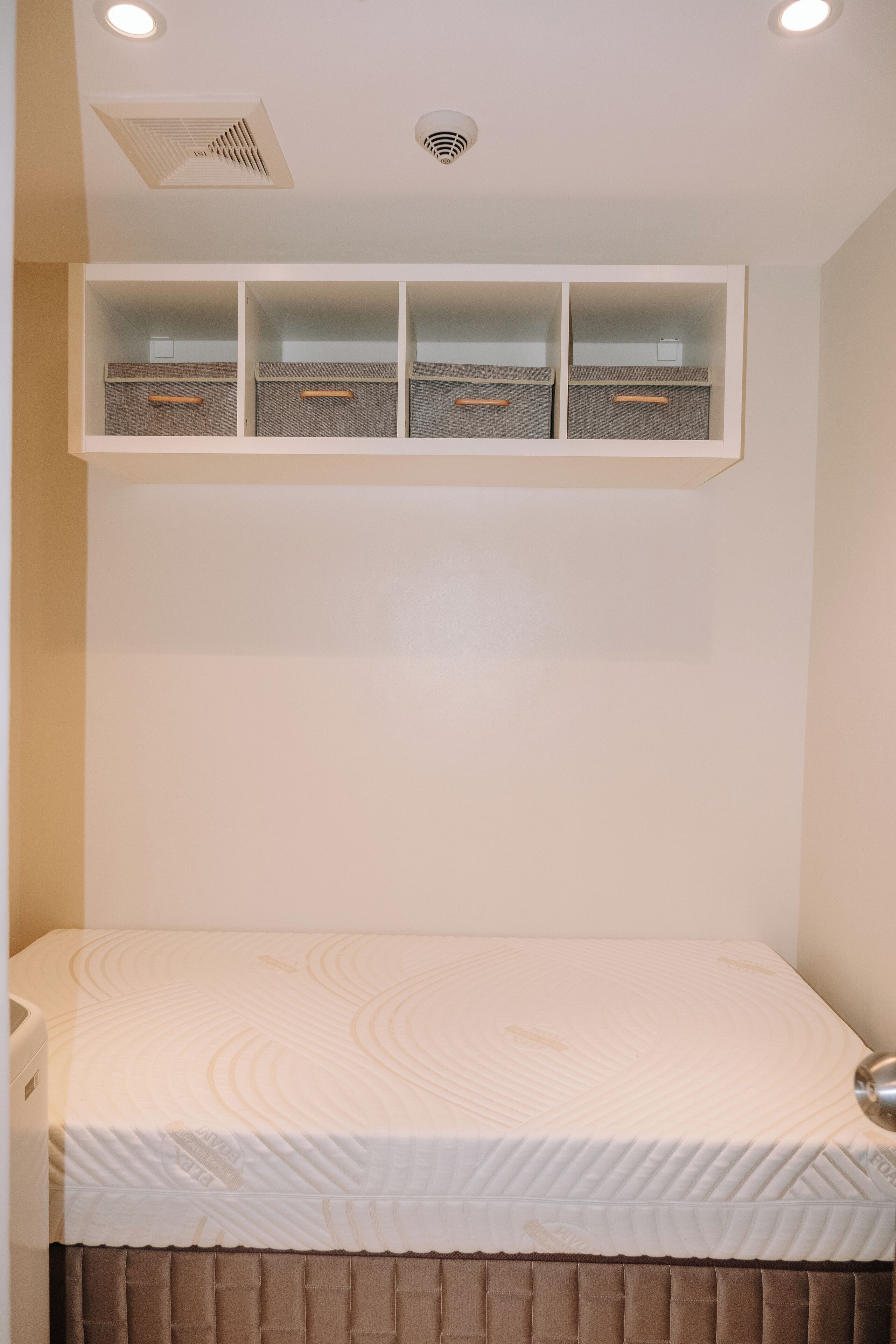 Ein Schlafzimmer mit einem Bett, einer eingebauten Ablage über dem Bett und einem Deckenlüfter.