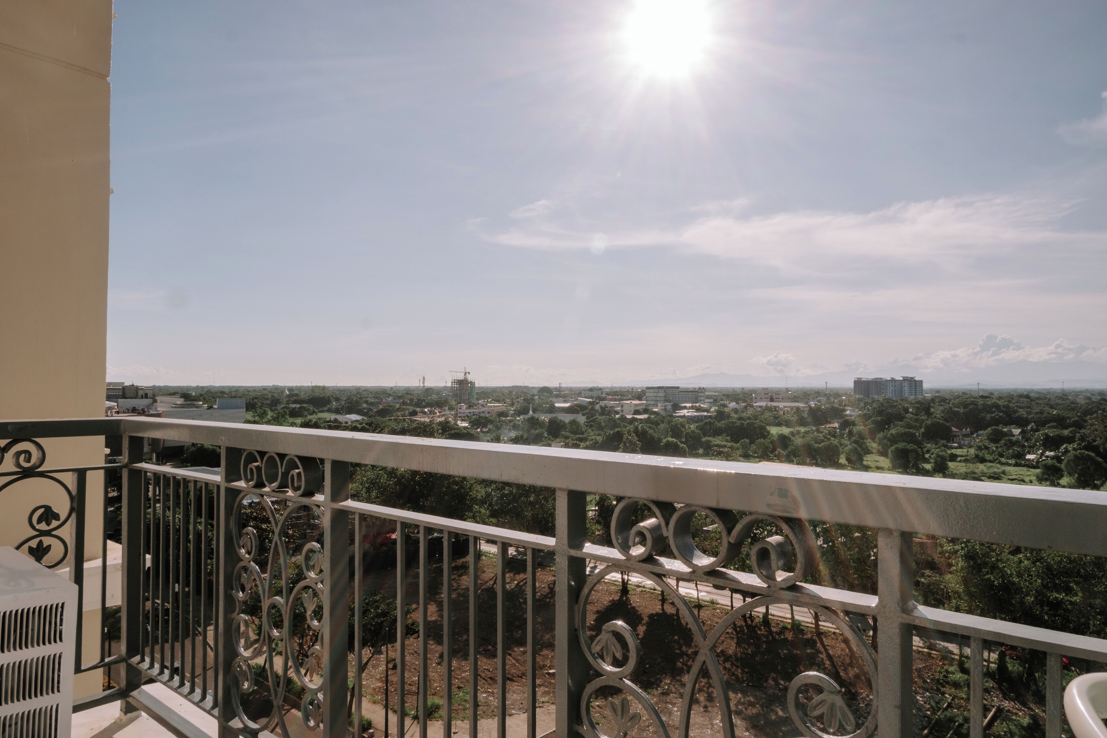 Ein Balkon mit Metallgeländer und Blick auf eine Stadtlandschaft mit Gebäuden und Grünflächen.