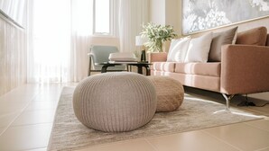 Un salon moderne avec un canapé beige, deux poufs ronds, une table d’appoint avec une lampe et un grand tableau abstrait accroché au mur.