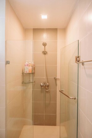 A glass-enclosed shower stall with beige tiles, a handheld showerhead, and a glass door with a silver handle. - A Warm & Cozy City Studio (Iloilo)