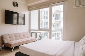 Un dormitorio moderno con una cama grande, un sofá, un televisor y un balcón con vistas a la ciudad.