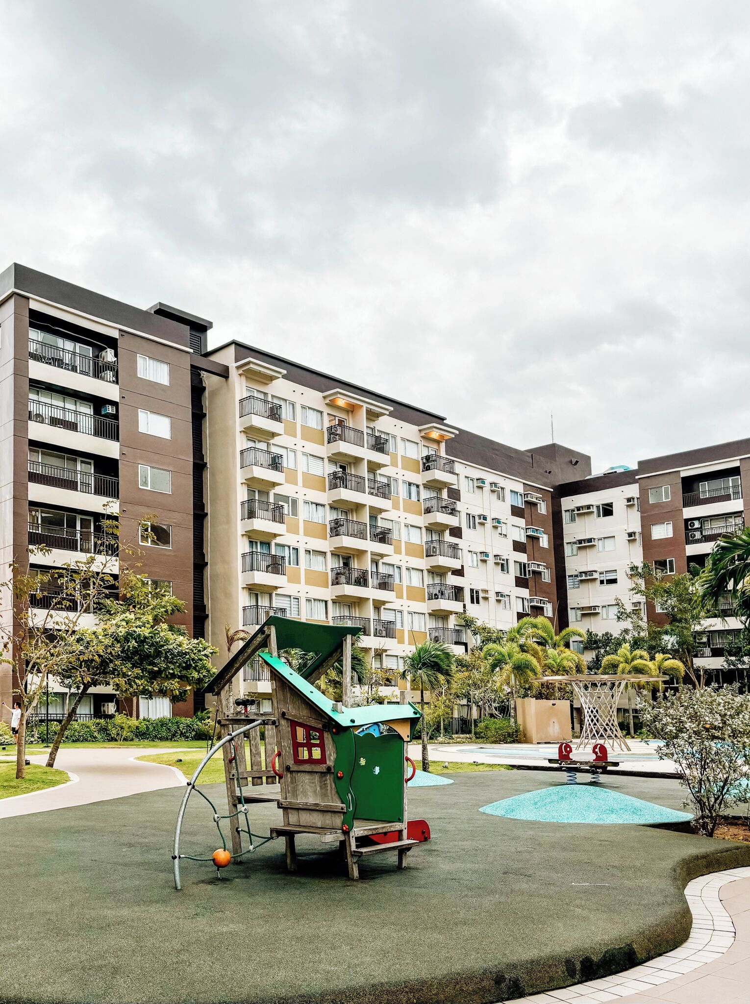Un terrain de jeux équipé d’un toboggan et d’une structure d’escalade, entouré d’un immeuble d’habitation doté de balcons et d’une piscine.