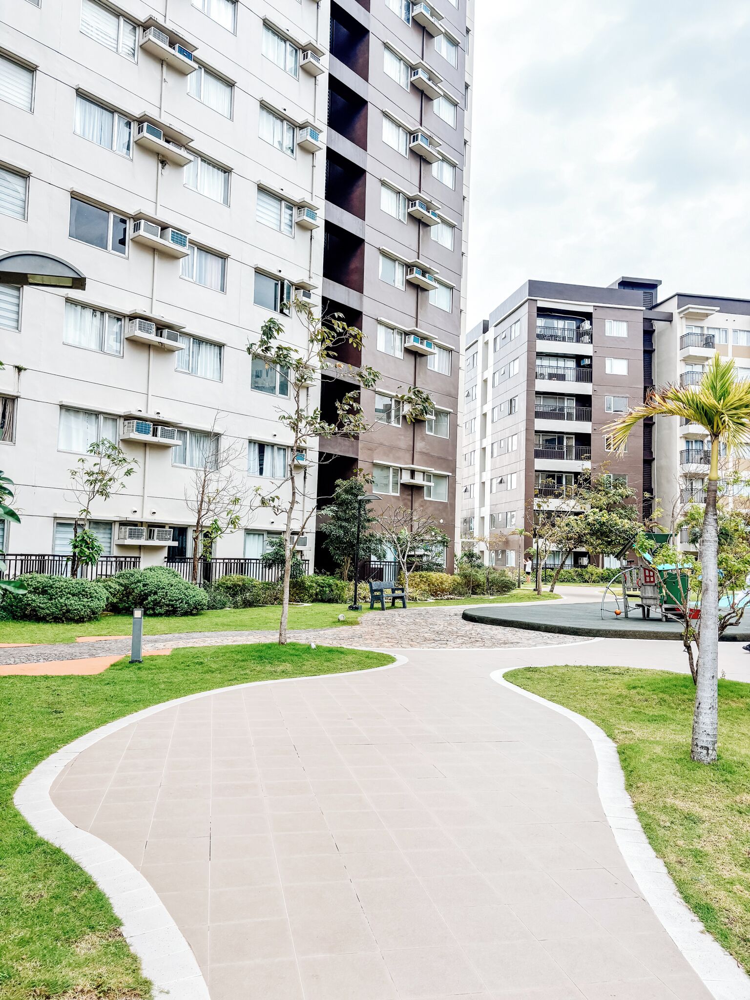 A residential building with multiple balconies, a paved walkway, and surrounding greenery.