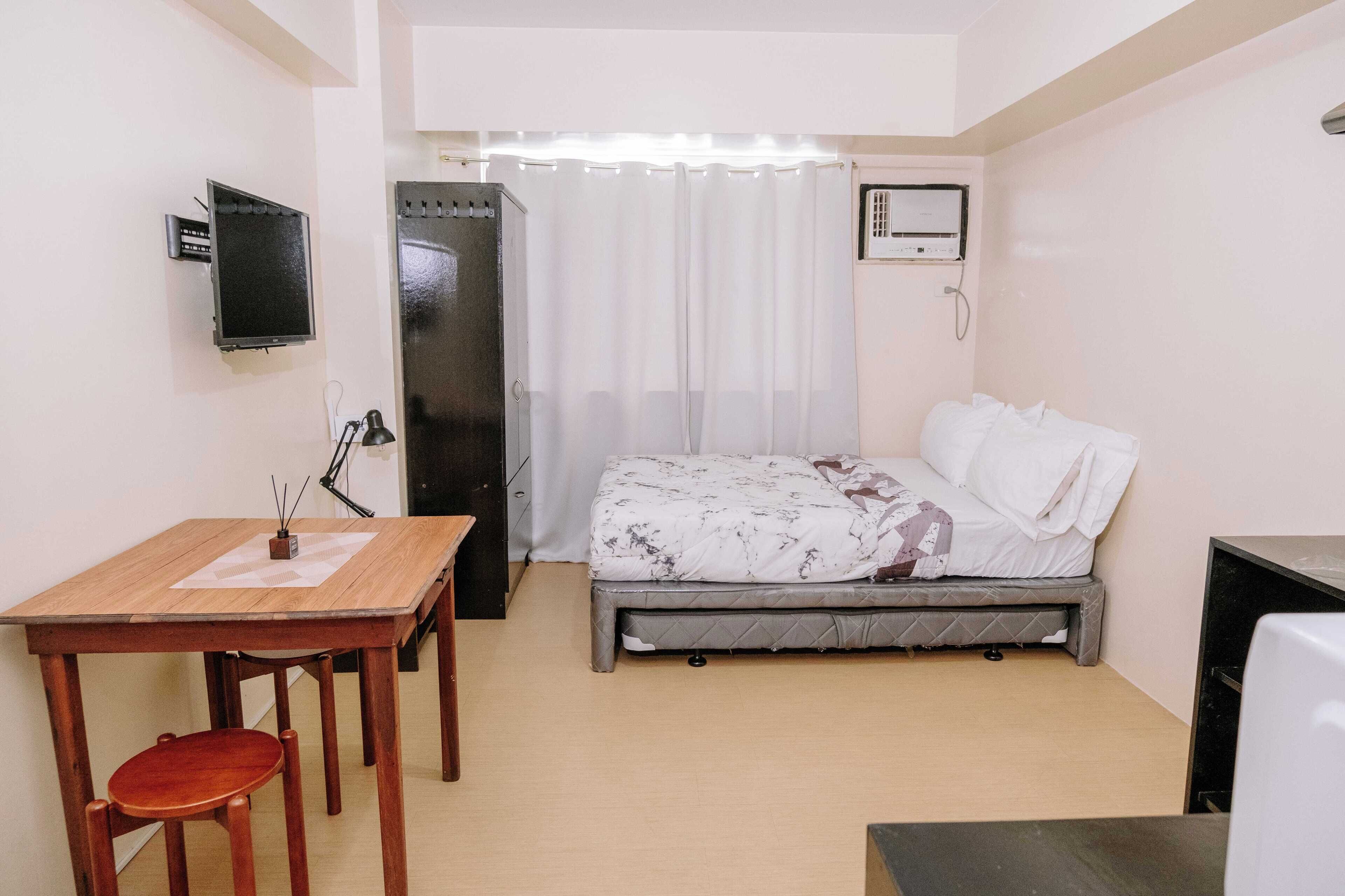 A small, clean room with a bed, a desk, a chair, a TV, and a shower area.