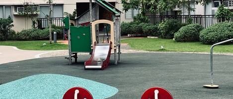 A playground with a seesaw and a slide in front of a residential building.