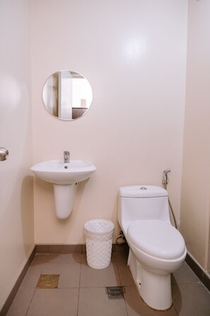 A small bathroom with a white sink, toilet, and a round mirror on the wall.
