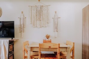 A wooden dining table with chairs, a TV on a stand, and macramé wall hangings.