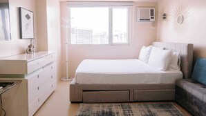 A modern bedroom with a large bed, a dresser, a sofa, and a window with a city view. - Simple Yet Stylish Escape (Iloilo)